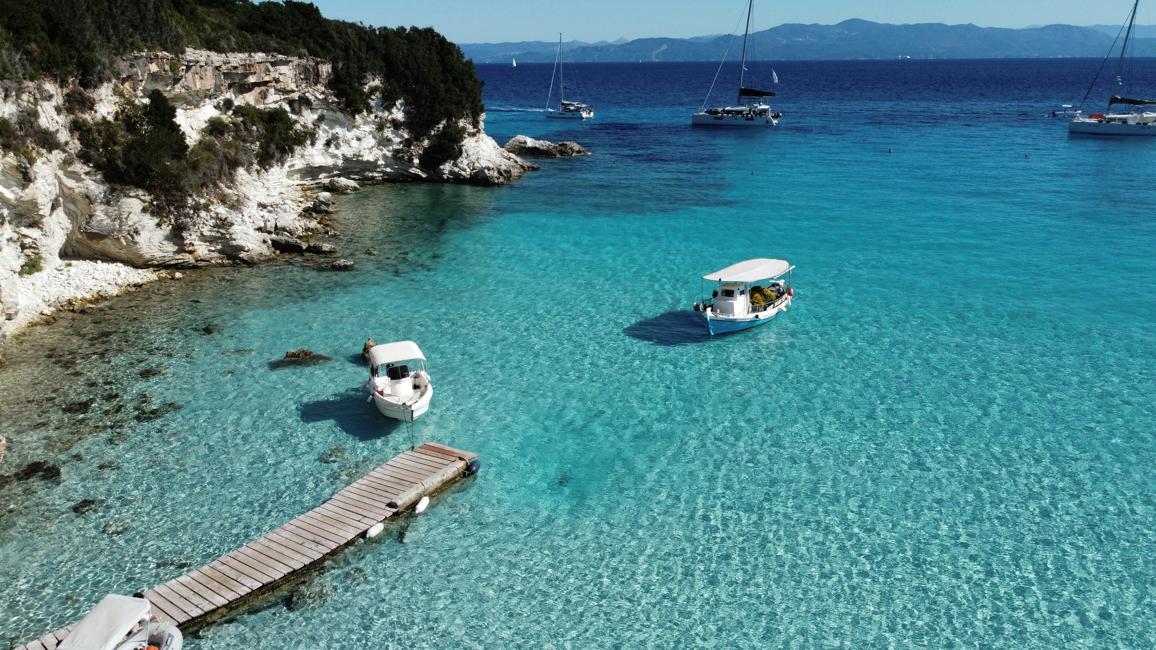 Crystal-clear turquoise water with small boats in a sheltered Greek cove