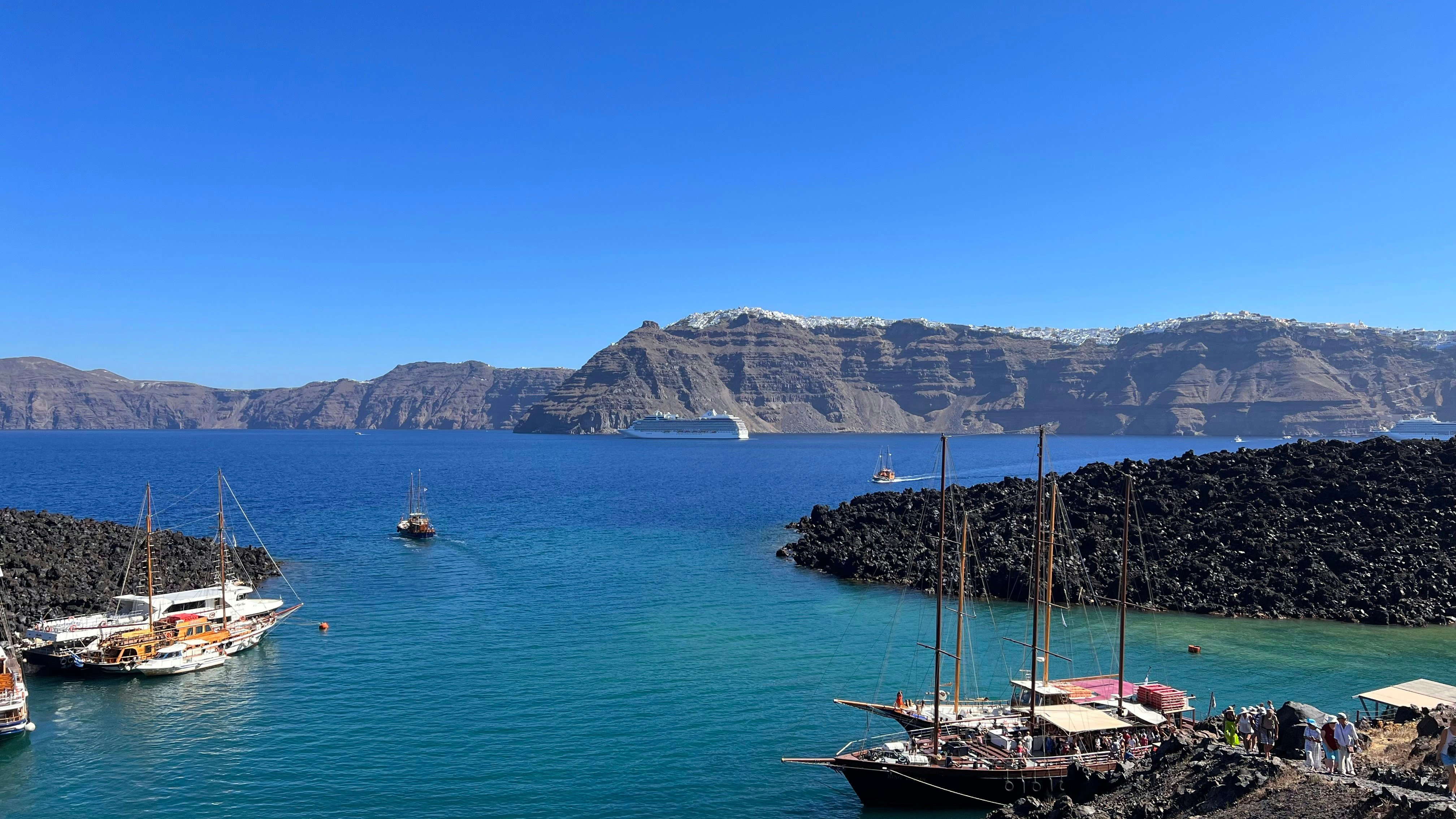 Boats moored in a Santorini harbour with the caldera cliffs behind