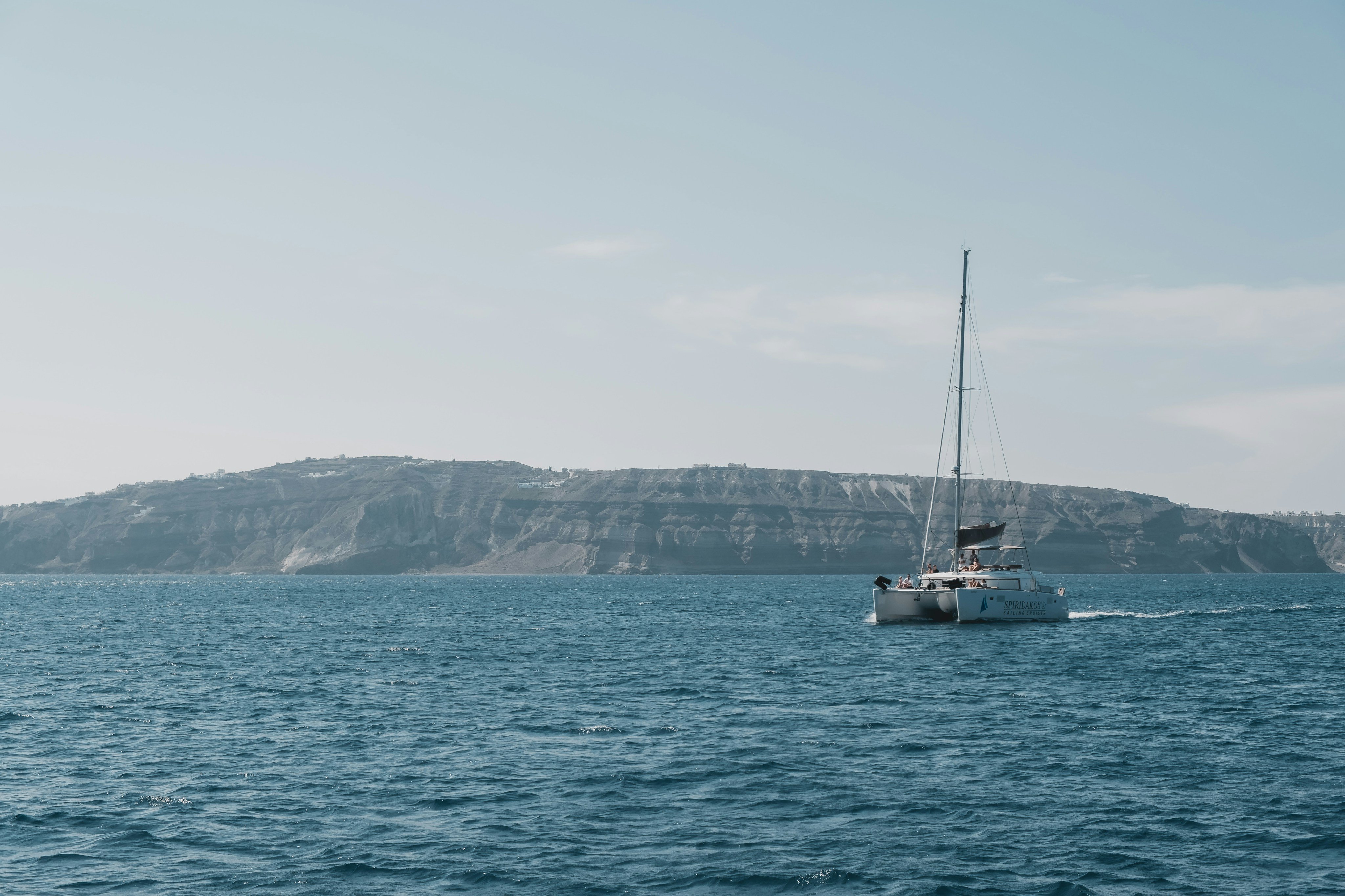 A catamaran on calm blue water near the white cliffs of Santorini