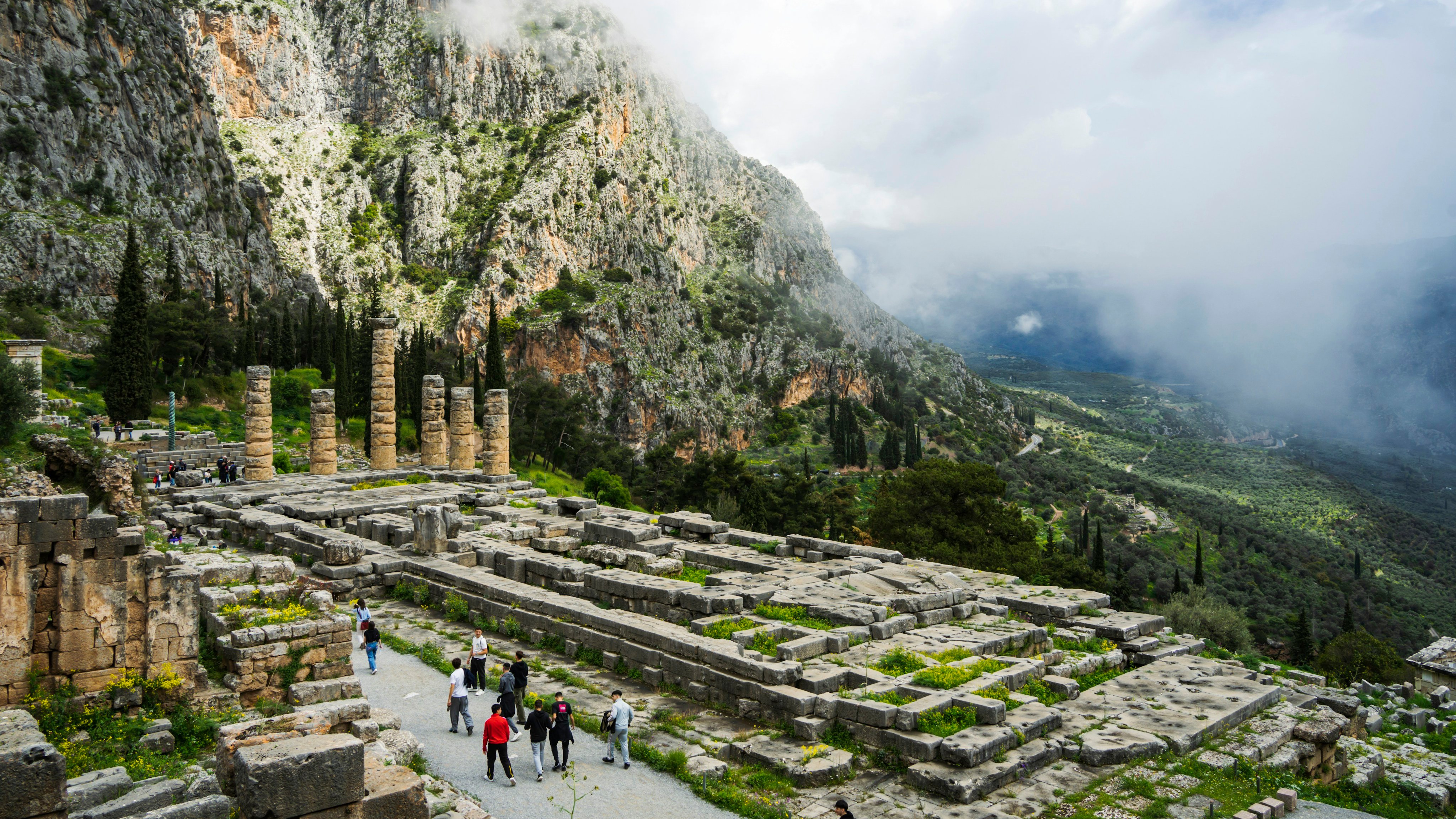 Visitors walking among ancient columns at Delphi with mountains behind
