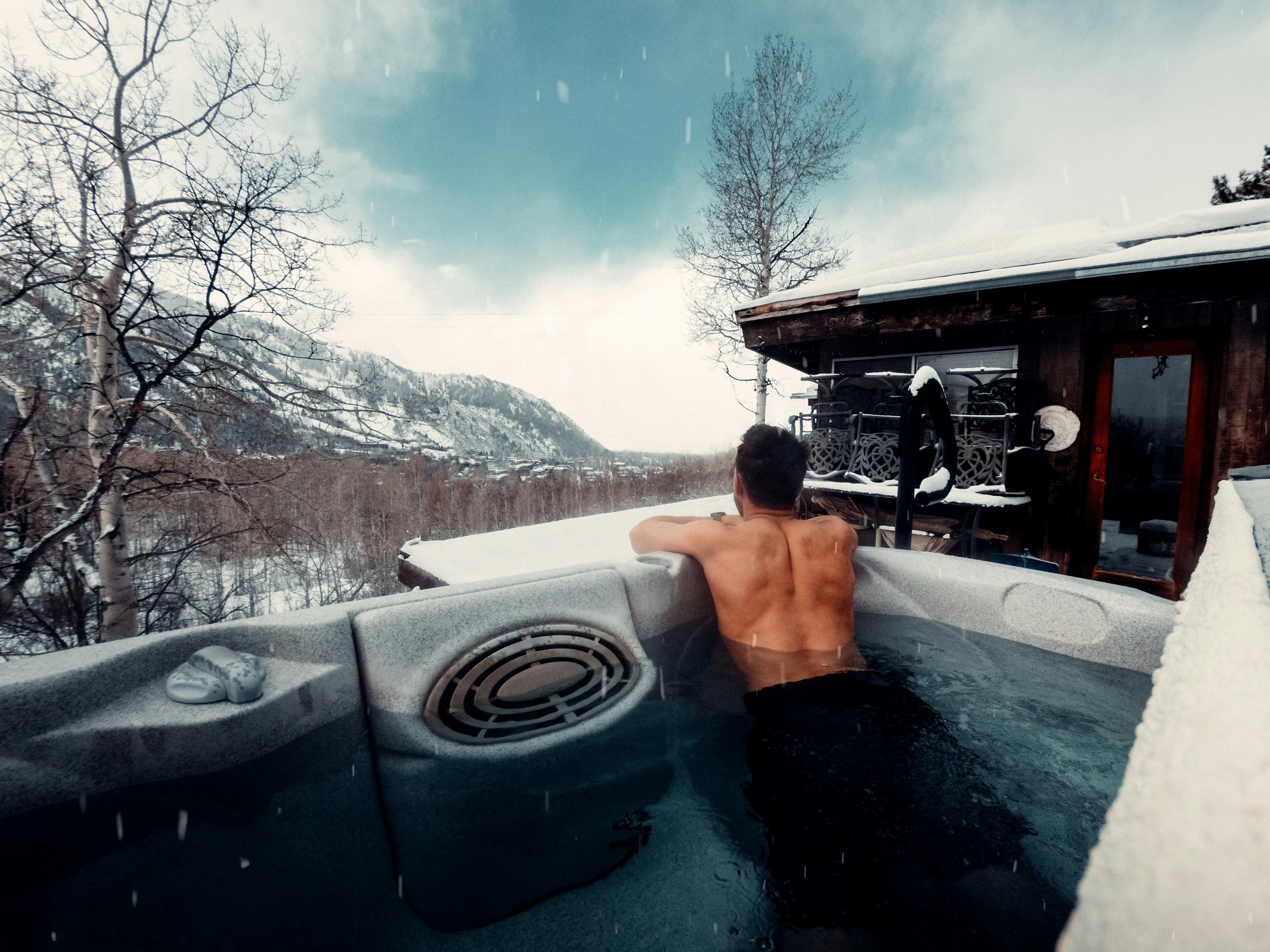 Steaming outdoor hot tub on a wooden deck at a Winter Park, Colorado house with snowy pines and a ridgeline behind