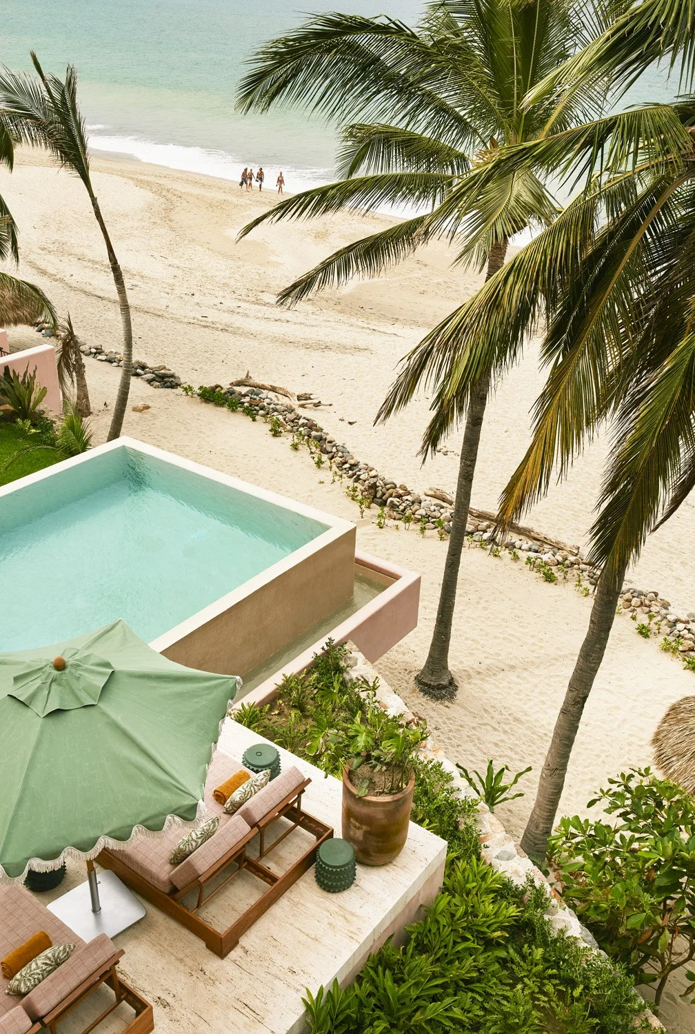 Beachfront property with turquoise pool, palm trees, lounge chairs, and sandy beach with ocean waves