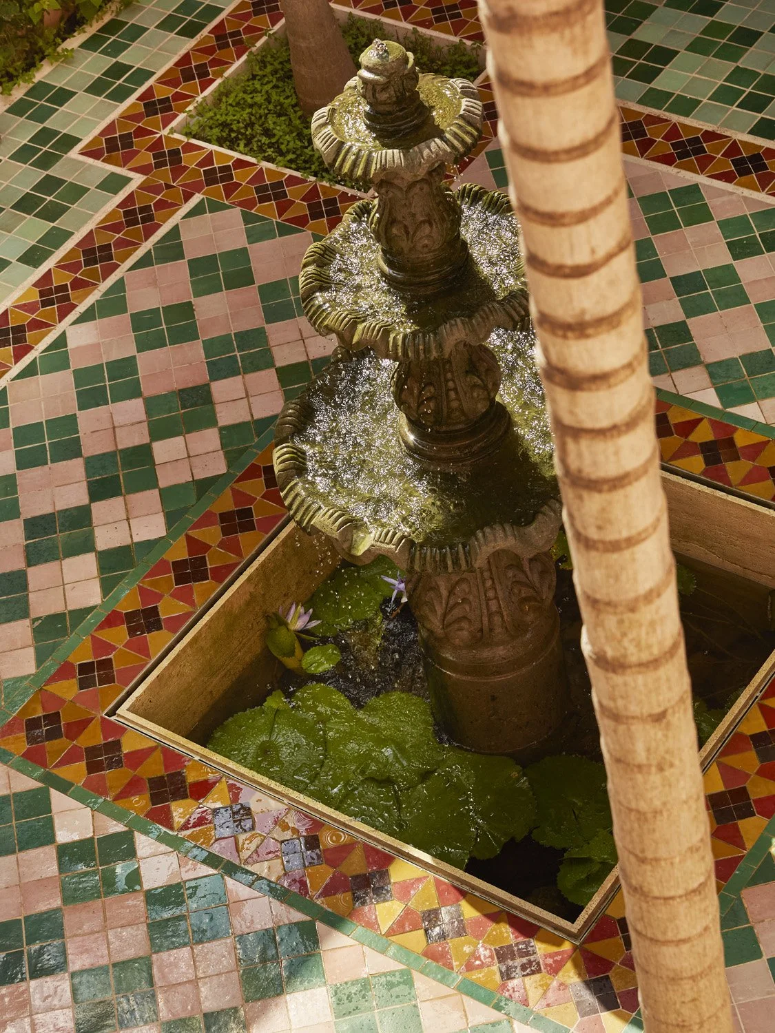 Ornate tiered fountain with carved stone base and brass details in geometric tile courtyard
