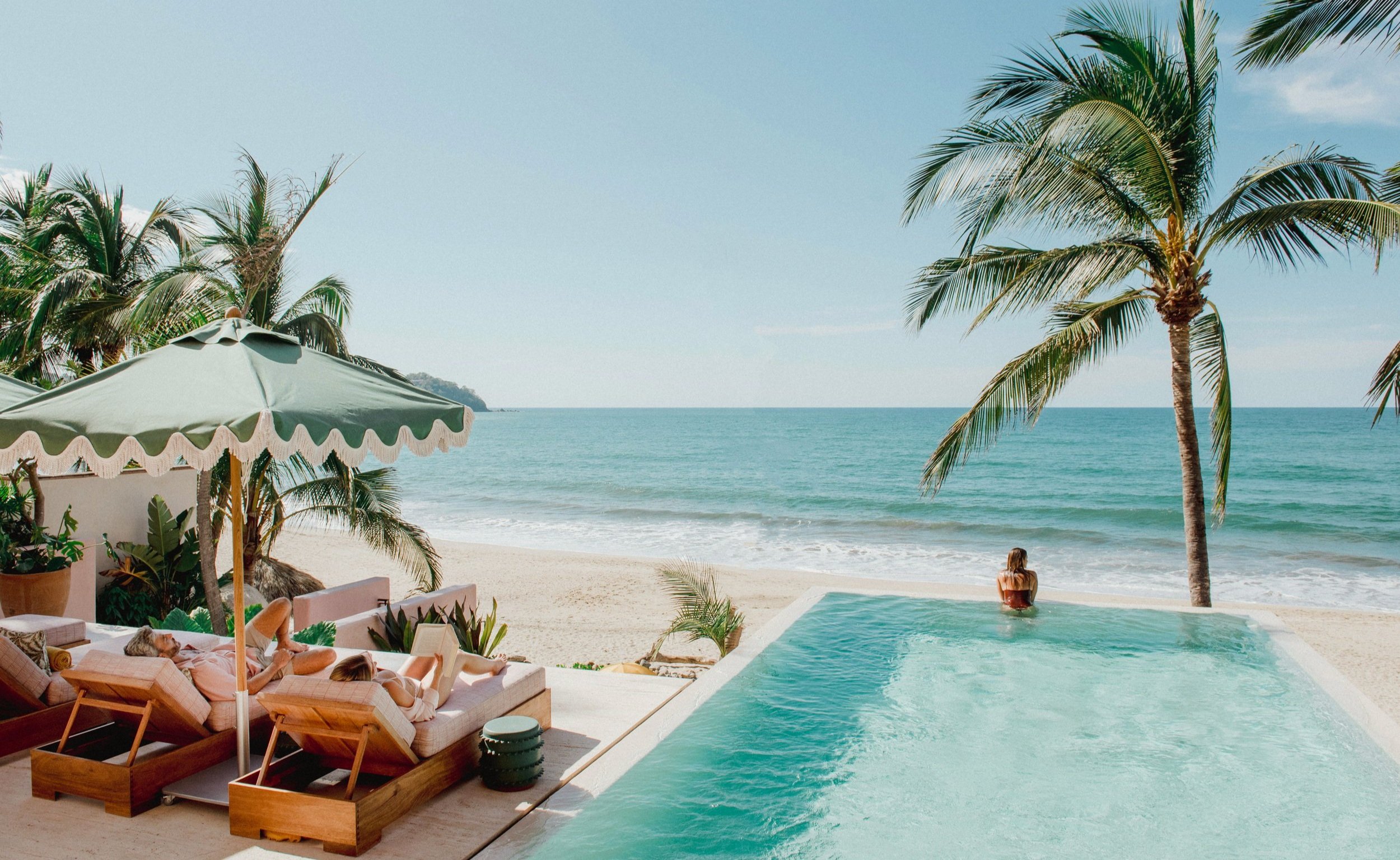 Beachfront infinity pool with loungers and umbrella overlooking turquoise ocean and sandy beach with palm trees