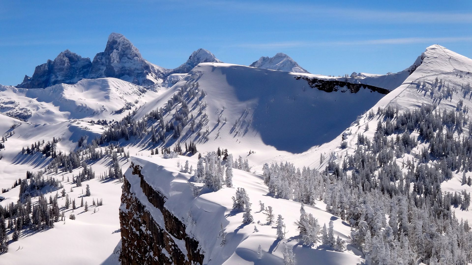 Snow-covered mountain peaks and forested slopes under clear blue sky