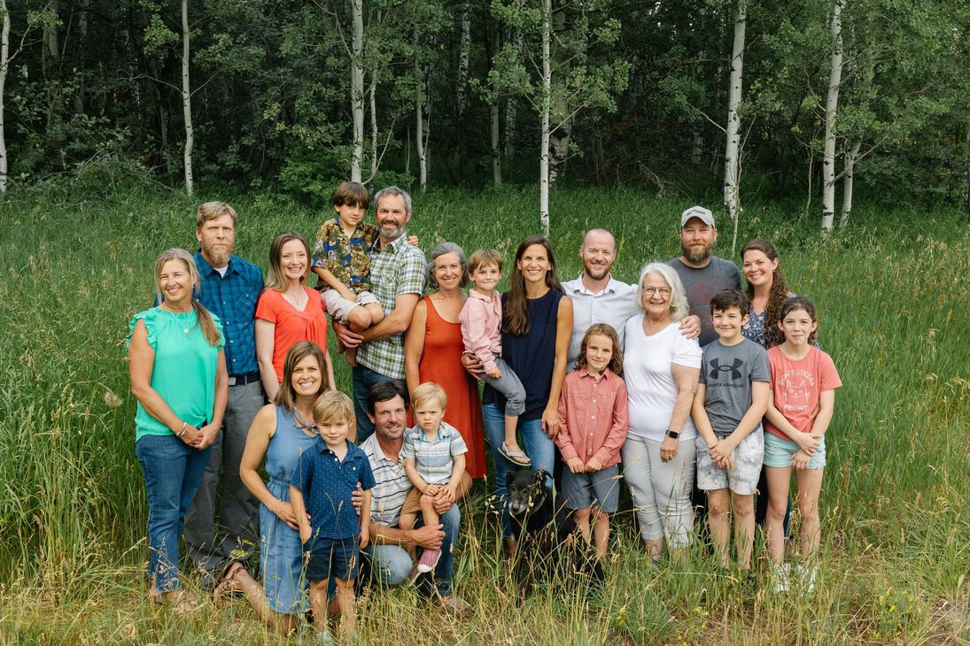 Large family group of adults and children standing together in a grassy field with birch trees in the background