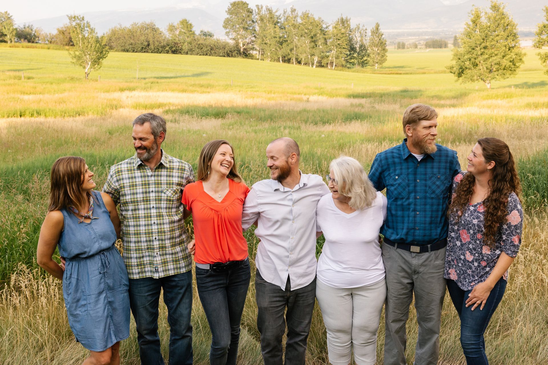 Seven people standing together in a grassy field with trees and rolling hills in the background.