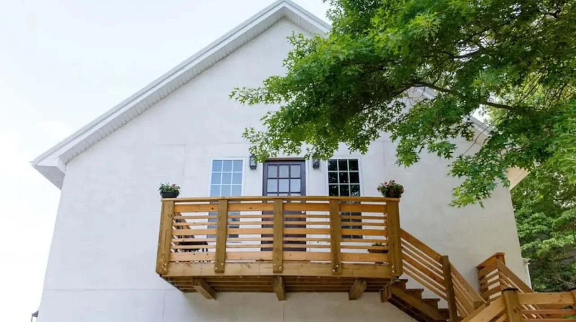 White house exterior with wooden deck, three windows, and overhanging tree branches